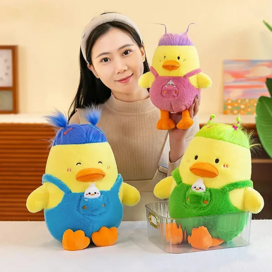 A smiling woman holding three duck cuddly toys dressed in pink, blue, and green overalls, featuring unique hairstyles and soft plush fabric